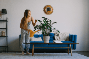 Mulher regando planta em sala de estar. Imagem ilustrativa para texto Vaso de planta para sala.